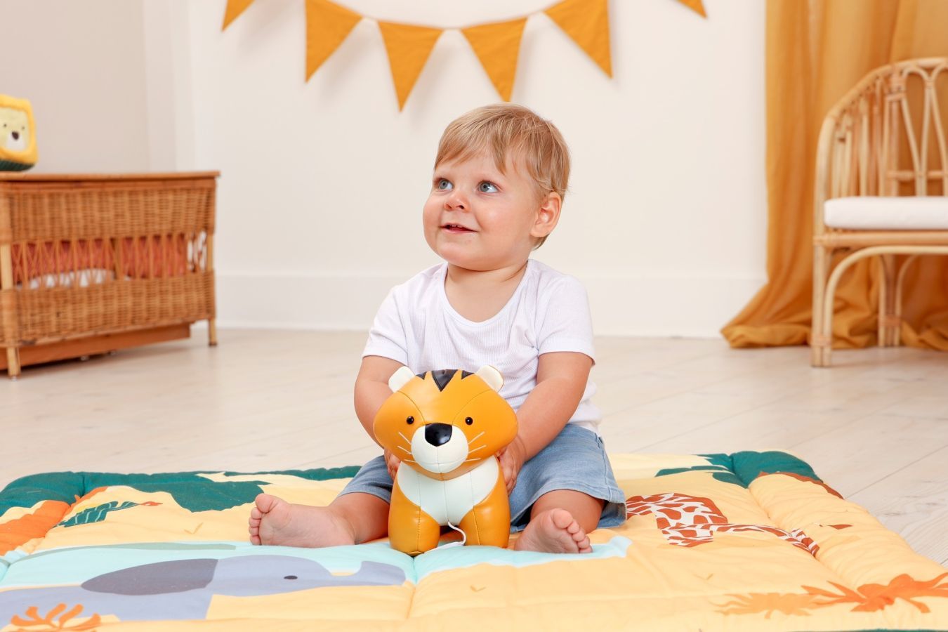 Bebé a brincar com brinquedo de peluche Little Big Friends tigre num tapete colorido.